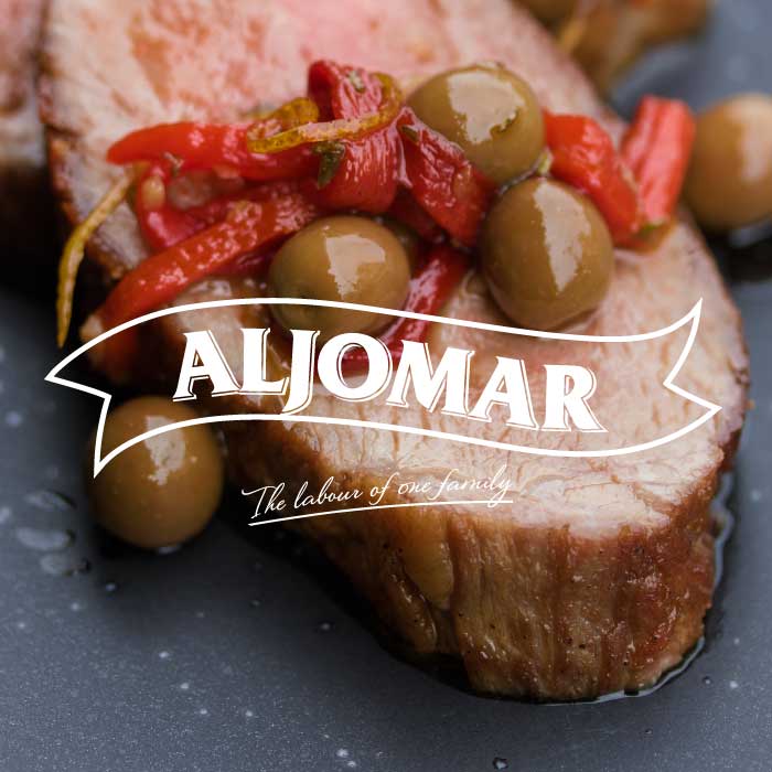 The Aljomar Iberico pork logo superimposed over cooked slices of Iberico pork presa topped with roasted red peppers and green olives.