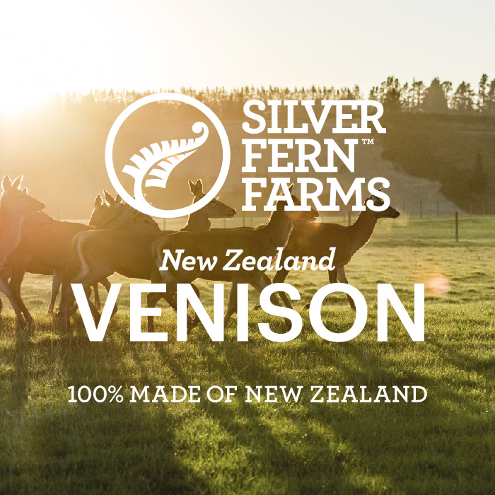 Silver Fern Farms logo superimposed over a herd of New Zealand venison crossing a grassy pasture with the sun setting in the background behind a forested hill.